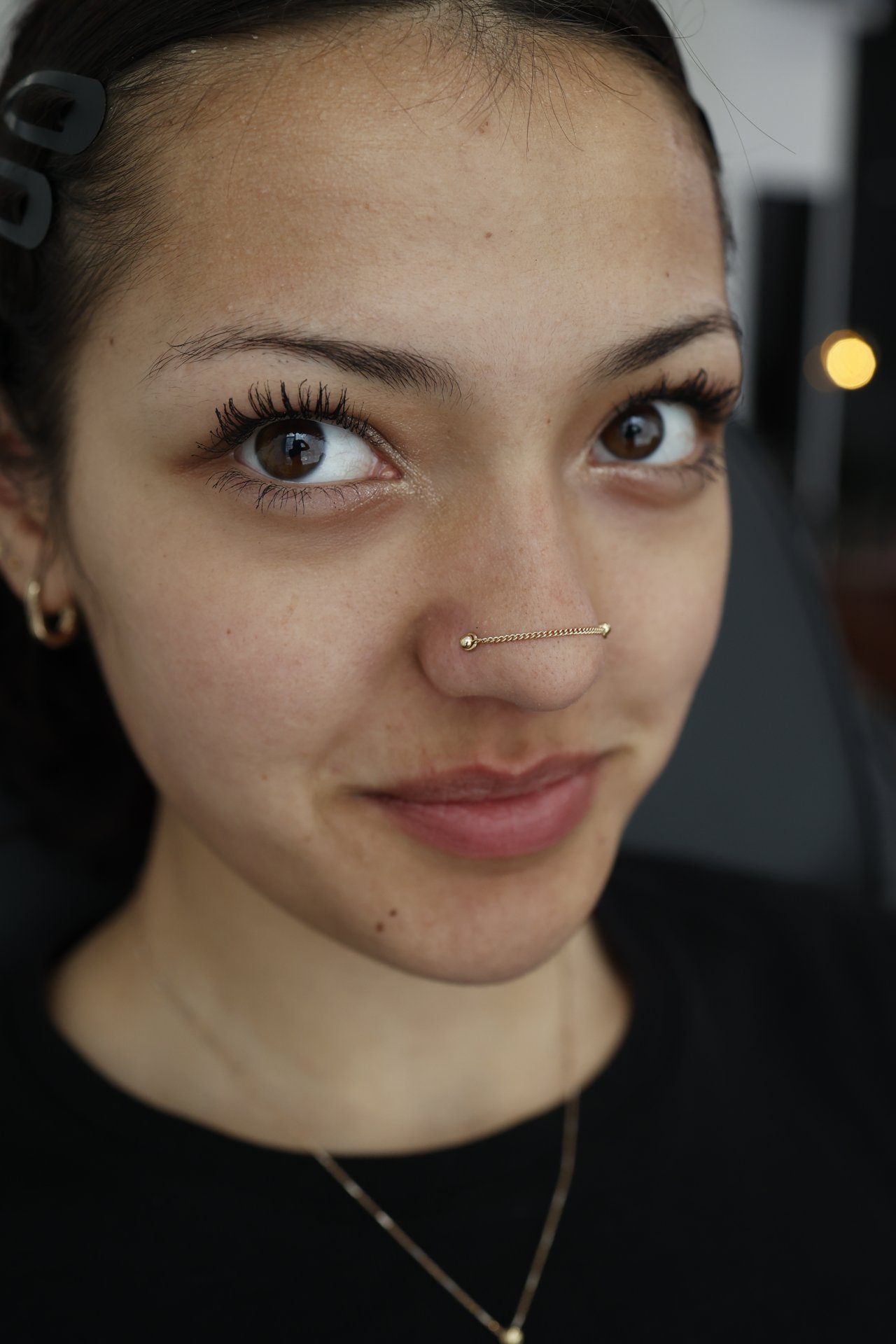 Editorial close-up of a gold nostril piercing in profile